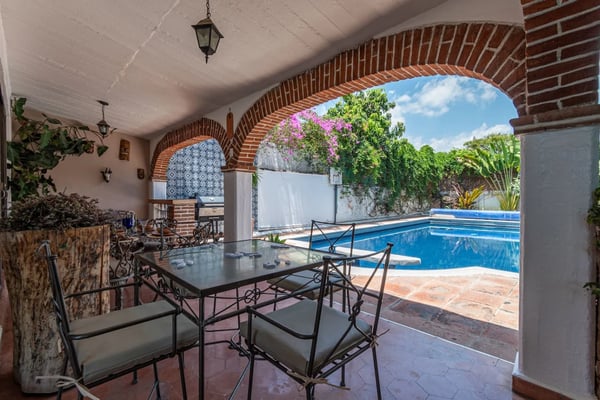 Covered patio with dining table overlooking swimming pool and flowering bougainvillea in walled garden